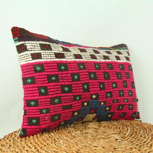 May include: A colorful rectangular pillow with a geometric pattern in shades of pink, brown, green, white, and blue. The pillow is made of woven fabric and has a fringed edge.