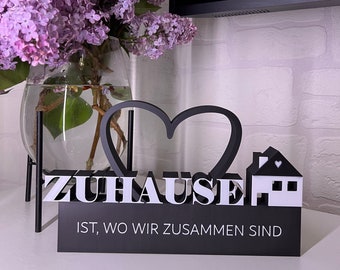 Puede incluir: Un letrero de madera negro con un corazón blanco y una casa blanca con un corazón en el techo. El letrero dice "ZUHAUSE IST, WO WIR ZUSAMMEN SIND".