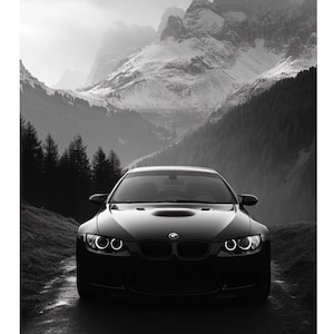 May include: Black and white framed print of a black sports car on a mountain road. The car is centered, with snow-capped mountains and a forest in the background. The image is a high-contrast, dramatic landscape.