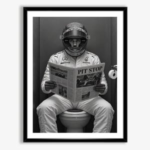 May include: A black and white framed print featuring a race car driver in a full racing suit and helmet sitting on a toilet while reading a newspaper titled PIT STOP. The suit displays Mercedes-AMG and Petronas logos on the chest.