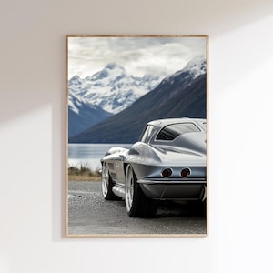 Könnte beinhalten: Ein silbernes Oldtimer-Auto, das auf einer Straße mit einem Gebirge im Hintergrund geparkt ist. Das Auto ist mit dem Heck zur Kamera gerichtet und die Berge sind mit Schnee bedeckt.