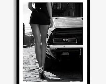 May include: Monochrome framed print showing a black classic car with "SS" lettering. A person in a black outfit and silver heels stands beside the car on a cobbled street.