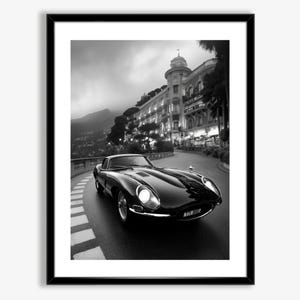 May include: A black and white photograph of a classic black Jaguar E-Type sports car driving on a winding road in front of a large building. The car is in focus, while the building and the road are blurred in the background.