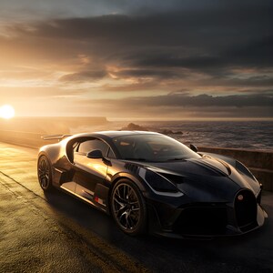 May include: A black sports car is parked on a coastal road at sunset. The car has a low profile, aerodynamic lines, and black alloy wheels. The sea and sky are visible in the background. The car's design is modern.