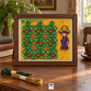 May include: A framed cross-stitch embroidery featuring a pixel art scene of a character wearing a straw hat and blue overalls standing next to a grid of green leafy plants on a yellow background, enclosed in a dark brown wooden frame.
