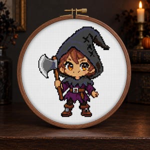 May include: A cross-stitch embroidery piece in a round wooden hoop featuring a pixel art character wearing a dark gray hooded cloak and a purple tunic. The character has brown hair, orange eyes, and holds a gray axe with a brown handle.