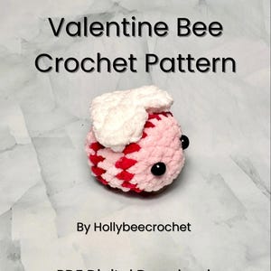May include: A crochet pattern for a Valentine's Day bee. The bee is pink and red with white wings and black eyes. The pattern is available as a digital download.  "Valentine Bee Crochet Pattern" and "By Hollybeecrochet" are written on the image.