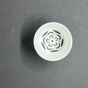 May include: White ceramic planter with a decorative black floral design. The planter has a round shape and a smooth surface.