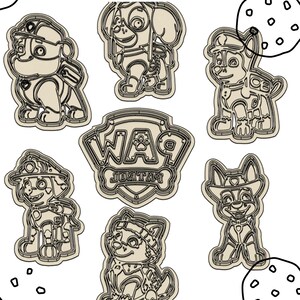 May include: A selection of cookie cutters depicting characters from Paw Patrol. The cutters are shaped like the characters and the Paw Patrol logo. The cutters are beige with detailed outlines.