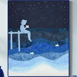 May include: Framed artwork showing a person silhouette on a pier, holding a star, with paper boats on the water. The art uses blue shades for the sea and sky, with a starry night. A decorative piece for a home.