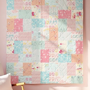 May include: A pink and white patchwork quilt with a variety of floral and animal prints hangs on a pink wall in a nursery. The quilt is made up of squares of different fabrics, each with a unique design. The quilt is a great addition to any nursery and would make a perfect gift for a new baby.