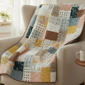Może przedstawiać: Patchworkowa kołdra w pastelowych odcieniach, narzucona na kremowy fotel. Kołdra składa się z wielu kwadratów z kwiatowymi i geometrycznymi wzorami. Krawędzie kołdry wykończone są brązową obwódką.