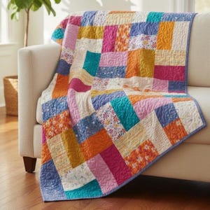 May include: A vibrant patchwork quilt in shades of pink, orange, blue, and yellow, draped over a cream sofa. The quilt is made of rectangular fabric patches with a blue border. The quilt is made of soft, textured fabric and is suitable for a double bed.