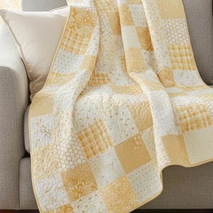 May include: A yellow and white patchwork quilt draped over a gray sofa. The quilt features various patterns, including gingham, floral, and dotted designs. The quilt is made of soft fabric and is a cozy home decor item.