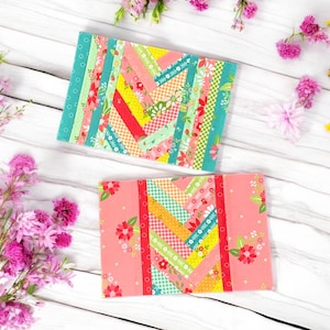 Pu&ograve; includere: Due quadrati di tessuto fatti a mano con un design a patchwork. I quadrati sono fatti di strisce di tessuto colorate in tonalit&agrave; di rosa, giallo, verde e rosso. Il tessuto &egrave; disposto in diagonale. I quadrati sono su uno sfondo di legno bianco.