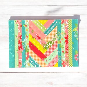 Pu&ograve; includere: Un blocco di trapunta patchwork colorato con un motivo a chevron. Il blocco &egrave; composto da strisce di tessuto in varie tonalit&agrave; di verde, rosa, giallo e rosso. Il tessuto presenta motivi floreali e geometrici.
