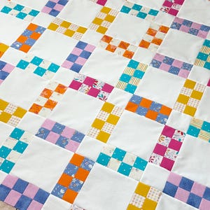 Könnte beinhalten: Eine handgefertigte Steppdecke mit Patchwork-Design. Die Steppdecke hat ein Rastermuster mit weißen Quadraten und farbigen Blöcken in Rosa, Blau, Orange und Gelb. Die Blöcke haben florale und geometrische Muster.