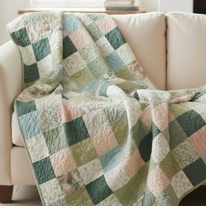 Puede incluir: Una colcha de retazos sobre un sofá crema. La colcha presenta un patrón de cuadrados en tonos verdes, rosas y azules. Los cuadrados tienen varias texturas y diseños, creando una estética acogedora y atractiva.