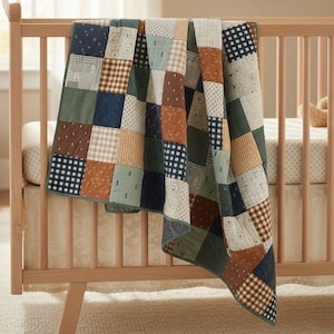 Könnte beinhalten: Eine Patchwork-Decke, die über einem Holzbettchen drapiert ist. Die Decke weist eine Vielzahl quadratischer Muster in Grün-, Braun-, Blau- und Beigetönen auf. Einige Quadrate haben Bären- und Tupfenmuster. Das Bettchen ist aus hellem Holz gefertigt.