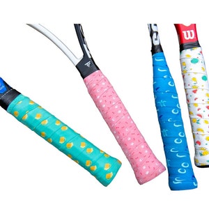 May include: Four tennis racket grips in various colors. One is light green with yellow beer mugs, another is pink with small white paw prints, a third is blue with white turtles, and the last is white with colorful fruit.
