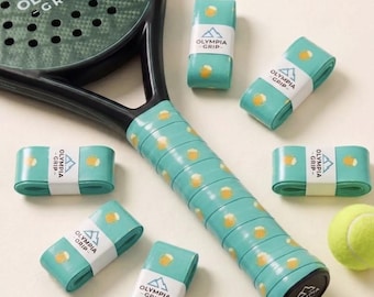 May include: A black padel racket with a green textured face and a light blue grip featuring a repeating beer mug pattern. Five additional light blue grip rolls with the same pattern and Olympia Grip branding are arranged around the racket.