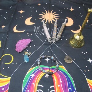 Peut inclure: Divers objets spirituels sur une tapisserie noire à motif céleste. Comprend des baguettes de cristal, une cloche en laiton, un bracelet et divers cristaux. La tapisserie présente un soleil, une lune, des étoiles et une illustration colorée.