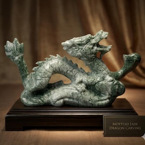 May include: A mottled green jade dragon carving featuring a serpentine body with detailed scales, an open mouth, and a raised tail. The sculpture is mounted on a rectangular dark wood base and includes a small plaque labelled MOTTLED JADE DRAGON CARVING.