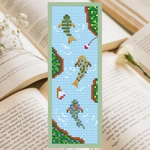 Peut inclure: Un marque-page en point de croix avec un fond bleu et une scène de rivière. Quatre poissons orange et verts nagent dans la rivière. La rivière est bordée d'herbe verte et de fleurs.