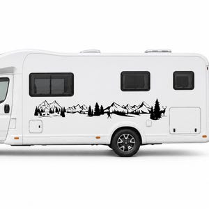 May include: A white recreational vehicle featuring a black adhesive decal on its side. The decal displays a detailed landscape illustration including jagged mountain peaks, dense pine trees, a small human figure, and a deer standing in profile.