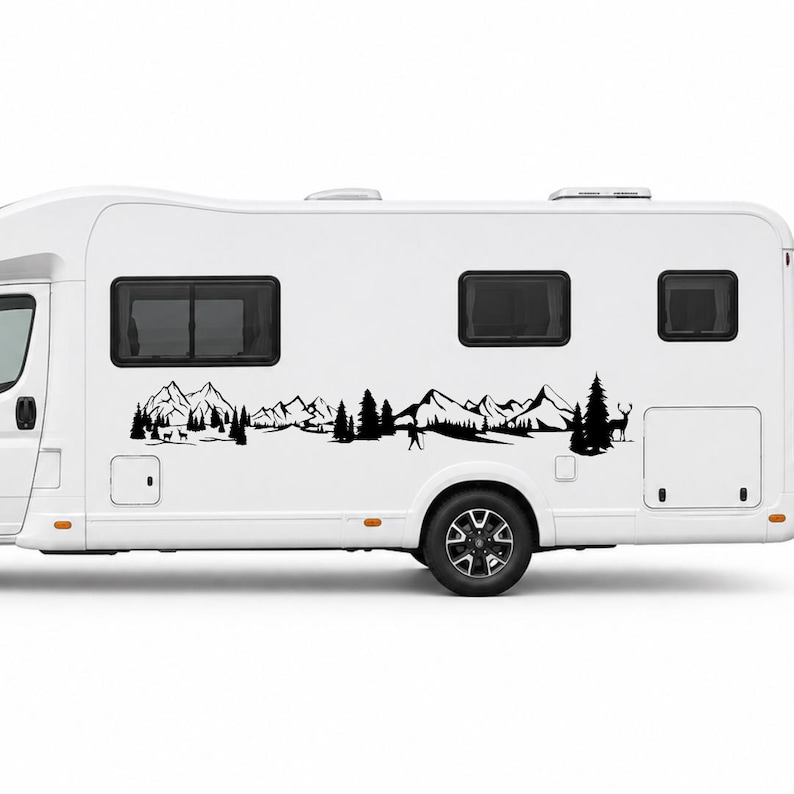 May include: A white recreational vehicle featuring a black adhesive decal on its side. The decal displays a detailed landscape illustration including jagged mountain peaks, dense pine trees, a small human figure, and a deer standing in profile.