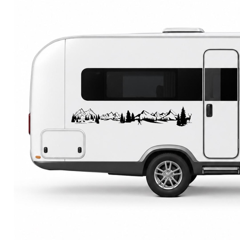 May include: A white camper trailer featuring a black vinyl decal of a mountain range landscape. The graphic includes silhouettes of jagged mountain peaks, dense pine trees, a small figure hiking with a pole, and a deer standing in the forest.