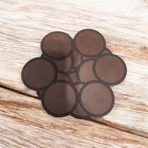 May include: A set of brown leather coasters with a rope design around the edge. The coasters are stacked on top of each other.