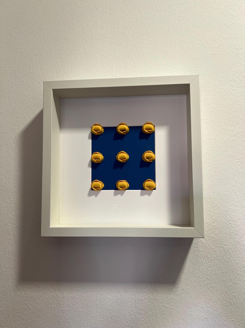 K&ouml;nnte beinhalten: Gerahmtes Kunstwerk mit neun gelben, halbkreisf&ouml;rmigen Objekten, angeordnet in einem 3x3 Raster auf einem dunkelblauen Hintergrund. Das Kunstwerk befindet sich in einem wei&szlig;en quadratischen Rahmen, an einer wei&szlig;en Wand.