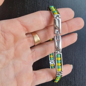 Könnte beinhalten: Ein silbernes Armband mit grünen und gelben Perlen. Das Armband hat einen Verschluss.