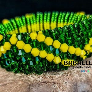 May include: A green and yellow beaded bracelet with a woven pattern. The bracelet is on a brown surface with the text "BABA ELEGUA Tienda esotérica" visible.