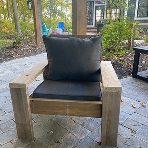Puede incluir: Una silla de madera con un coj&iacute;n gris y una almohada gris. La silla est&aacute; en un patio con suelo de ladrillo.