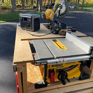 May include: A yellow and black DeWalt table saw with a gray table top and a silver fence. The saw is mounted on a wooden table with a black power cord running to a gray generator.