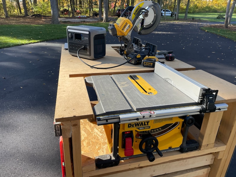 May include: A yellow and black DeWalt table saw with a gray table top and a silver fence. The saw is mounted on a wooden table with a black power cord running to a gray generator.