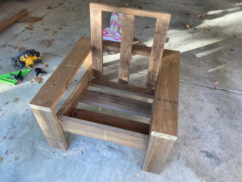 Puede incluir: Un marco de silla de madera con respaldo y asiento de listones. La silla est&aacute; sin terminar y tiene un color de madera natural.