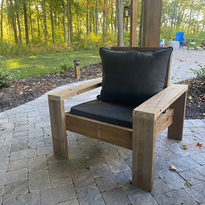 Puede incluir: Una silla de madera con un coj&iacute;n gris oscuro. La silla est&aacute; en un patio con un camino de piedra.