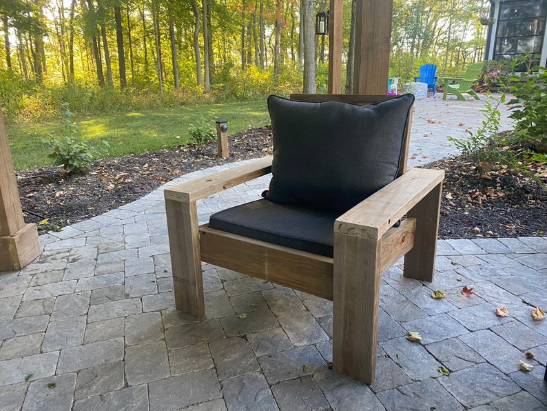 Puede incluir: Una silla de madera con un coj&iacute;n gris oscuro. La silla est&aacute; en un patio con un camino de piedra.