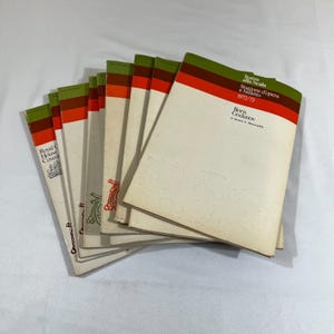 May include: A collection of vintage opera and ballet programs featuring off-white covers with horizontal green and orange stripes at the top. The front program displays the text Teatro alla Scala, Stagione d'opera e balletto 1972/73, and Boris Godunov.