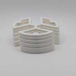 May include: White plastic stacking shims with the text "OFC STACKSTOP" and measurements of 4mm, 5mm, 6mm, 7mm, and 10mm. The shims are in a semi-circular shape with a triangular design. The background is plain white.