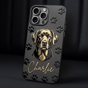May include: A black smartphone case featuring a raised gold-toned illustration of a dog's face in the center, surrounded by embossed paw prints. The name Charlie is written in a gold cursive script below the dog illustration.