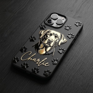 May include: A matte black smartphone case featuring a raised, metallic gold illustration of a dog's head and the name Charlie in cursive script. The case is decorated with multiple embossed black paw prints scattered across the surface.