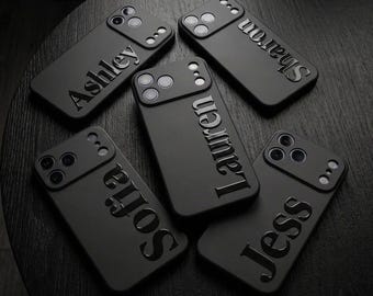 May include: Five matte black smartphone cases arranged in a circular pattern. Each case features a raised, glossy name embossed vertically on the back: Ashley, Sharon, Lauren, Sofia, and Jess. The cases have a cutout for a triple-lens camera system.
