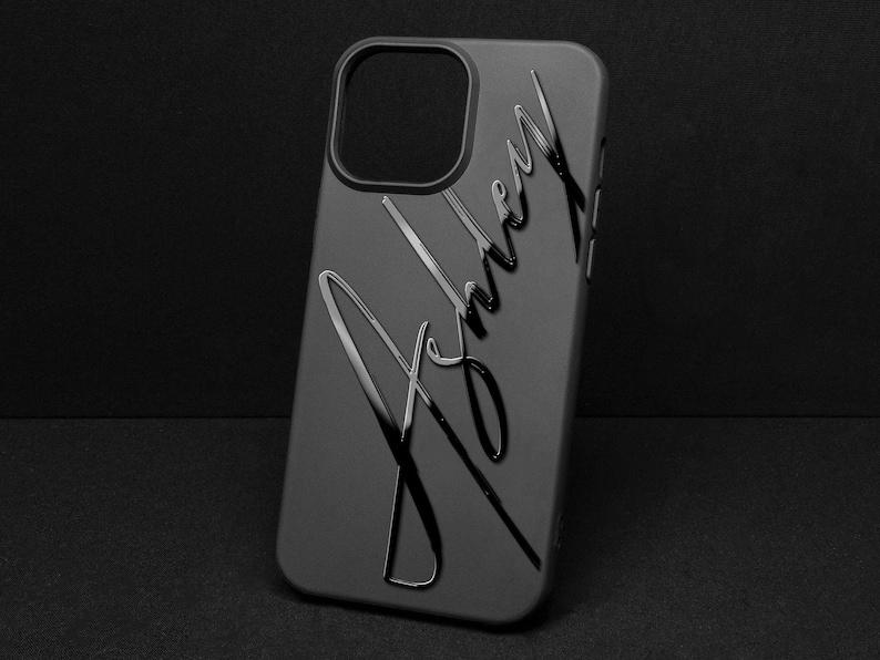 May include: A black phone case with the name "Ashley" in a cursive font. The case has a glossy finish and a camera cutout. The background is a solid black.