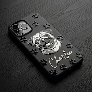 May include: A black smartphone case featuring a raised silver illustration of a pug dog face. The case is decorated with multiple small, raised black paw prints and the name Charlie written in a silver cursive script font on the back surface.