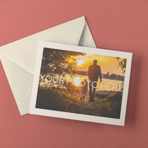 May include: A greeting card with a photograph of a person and child walking towards the sunset, with the text "YOUR PHOTO HERE". The card is accompanied by a cream-colored envelope, all set against a muted red background.