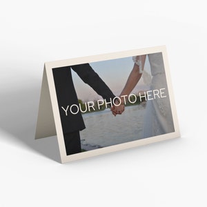 May include: A folded cream-colored card with a photograph of a couple holding hands. The photo has the text "YOUR PHOTO HERE" in white. The background of the photo shows a body of water and a blurred landscape.